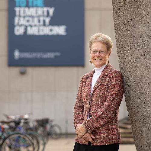 Patricia Brubaker smiles as she leans on the sculpture in front of the Medical Sciences Building at U of T.