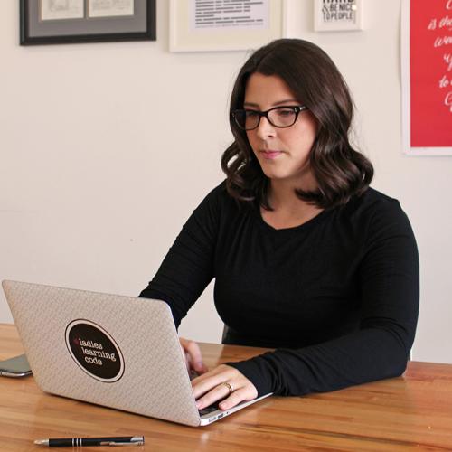 Melissa Sariffodeen types intently on a laptop. The laptop has a big sticker that reads Ladies Learning Code.