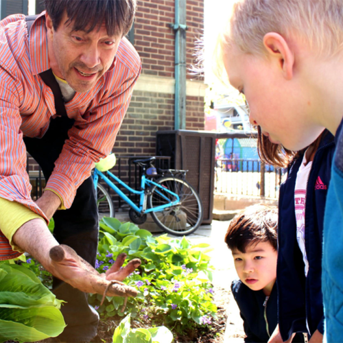 Standing in a garden, Doug Anderson shows children his hand filled with soil and a worm.