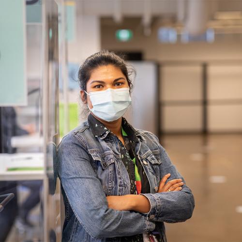 Upasana Saha, wearing a mask, stands in a hallway.
