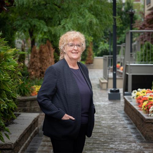 Ellen Hodnett smiles as she stands on a cobbled alleyway lined with gardens.