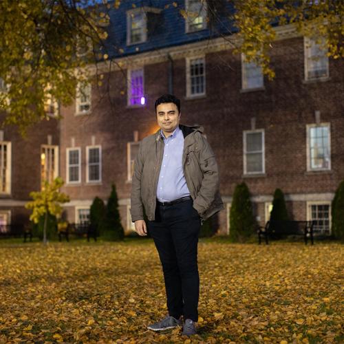Saad Shahid Shafiq smiles as he stands in a  leafy U of T quad at night.