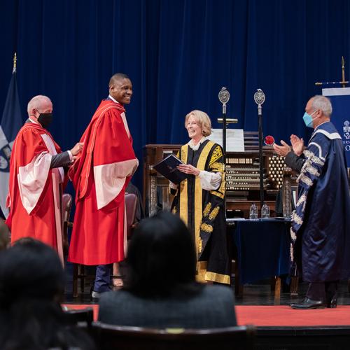 Masai Ujiri smiles as university officials place his academic hood over his head, on stage at Convocation Hall.