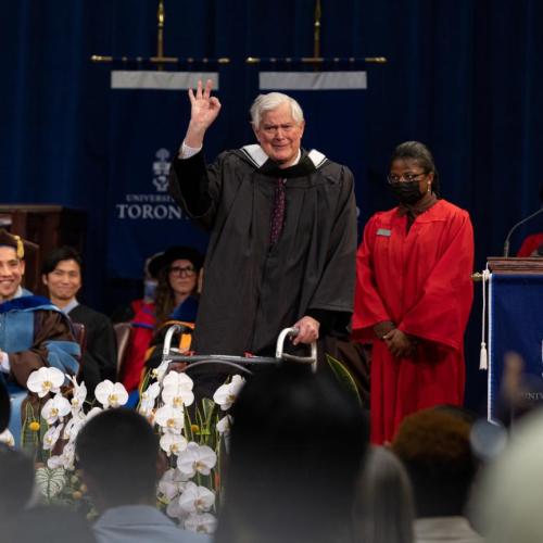 John Bond on the stage at graduation, making an OK sign with his hand