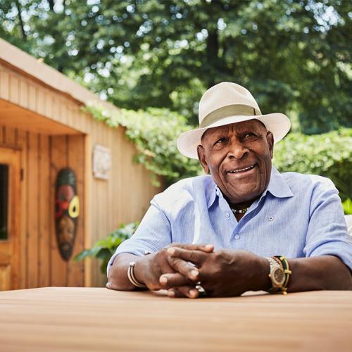 Denham Jolly smiles, sitting at a table on a backyard patio.