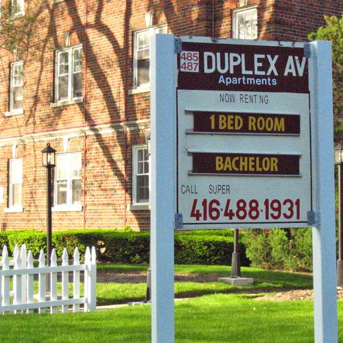 A sign outside a brick building reads: 485/487 Duplex Ave, now renting, 1 bedroom, bachelor, call super 416-488-1931.