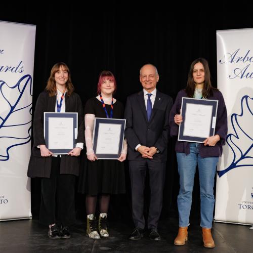 Three awards winners standing together with U of T president Meric Gertler, smiling and holding their awards..
