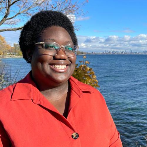 Marquela Nunes smiles happily, standing on the shores of a lake.
