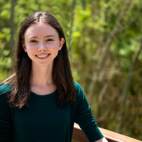 Abigail Clapperton smiles while standing on a boardwalk in a forest.