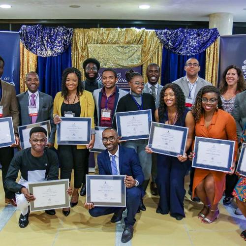 A group of 15 people pose holding framed African Scholars Awards certificates.