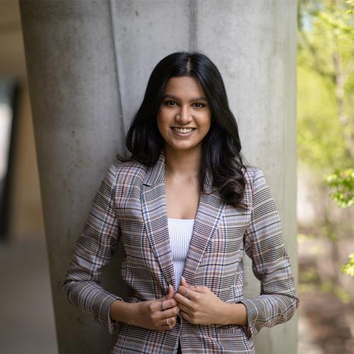 Aishwarya Nair smiles as she stands under the portico of a concrete building, next to a garden.