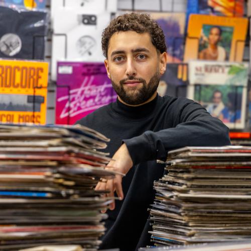 Amir Alam posing behind two tall piles of vinyl records