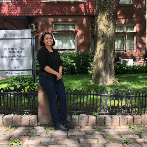 Ana Chiguichon smiles, standing on the sidewalk in front of a sign that reads, Transitional Year Programme.