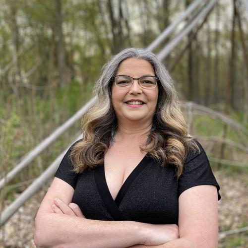 Angela Mashford-Pringle smiles as she stands outdoors in a forest.