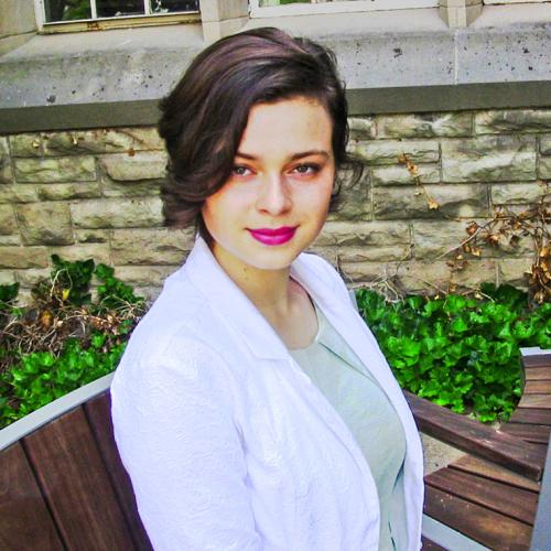 Anna Paliy smiles, sitting on a bench by an ivy-covered wall.