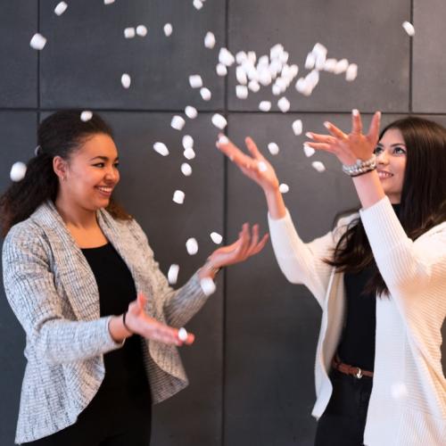 Anne Ageh and Nuha Siddiqui laugh together as they toss biodegradable packing peanuts in the air.