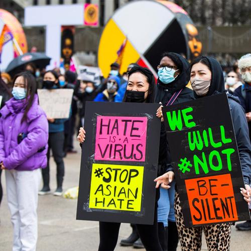 A crowd of people in masks at a protest hold signs that read: Hate is a Virus, Stop Asian Hate, We will not be silent.