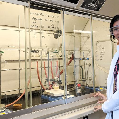 Avneet Ghotra, wearing safety goggles and lab coat, stands in front of an array of taps, hoses, beakers and clamps.
