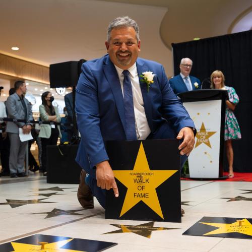 Andrew Arifuzzaman smiles happily, kneeling on a pavement with star-shaped tiles: Scarborough walk of fame.