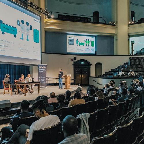 An audience in Convocation Hall watches a presentation on clean energy startup Reeddi.