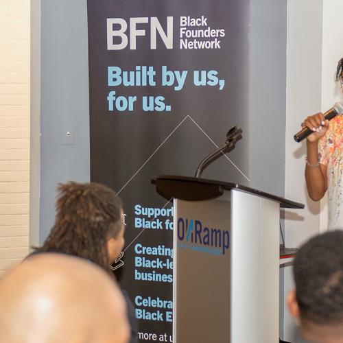 Rhonda McEwen speaks in front of a sign that says: BFN, Black Founders Network, built by us, for us.