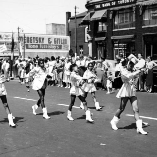 Young Black girls, wearing majorette costumes, march in a parade, in an old photo from the 1950s.
