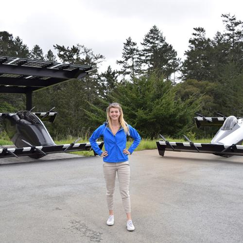 Kristina Menton stands in front of two vehicles that look like race cars with no wheels and very long, wide, flat axles.