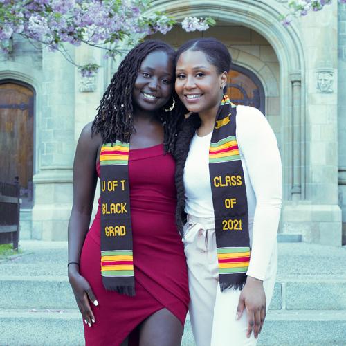 Cindy Njoki Kamau and Debora Oresajo smile together, wearing kente scarves that read: U of T Black Grad Class of 2021.