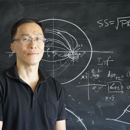 Willy Wong stands in front of a blackboard covered with an oval-shaped diagram and mathematical formulae.