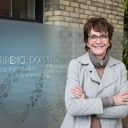 Brenda Andrews smiles as she stands beside a sign reading Terrence Donnelly Centre for Cellular and Biomolecular Research