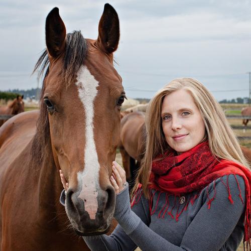 Carolyn Creed smiles as she pets a horse's face in an outdoor paddock.