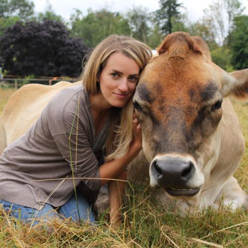Camille Labchuk  hugs a cow that is lying crouched in a field.
