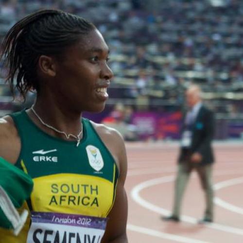 Caster Semenya smiles and waves the South African flag while standing on the track in a stadium.