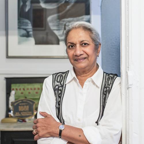 Ceta Ramkhalawansingh smiles, leaning in a doorway near a desk holding memorabilia.