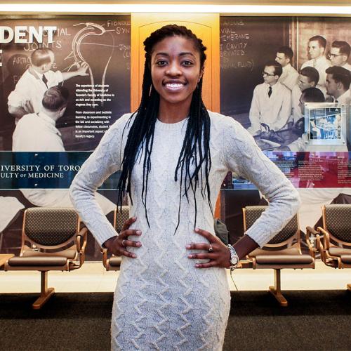 Chika Oriuwa smiles happily, standing in front of a display about the history of Student Life at the Faculty of Medicine.