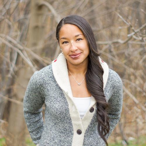 Cylita Guy smiles, standing in a park before leafless trees.