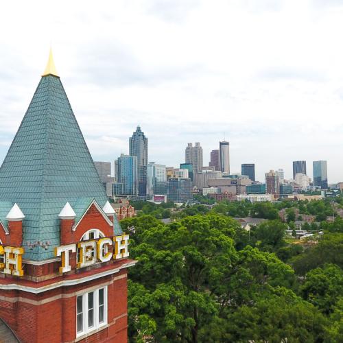 The word TECH is blazoned on the roof of a tower overlooking a forested city campus.