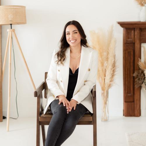 Portrait of Lauren Watkins sitting in a chair and wearing a white blazer