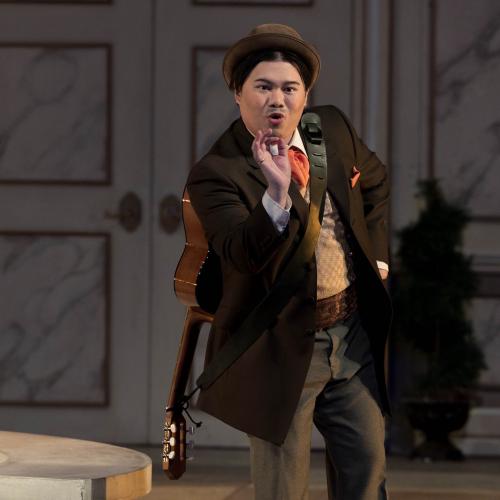 Danlie Rae Acebuque in costume as Figaro. He is singing and gesturing, wearing a guitar slung on his back.