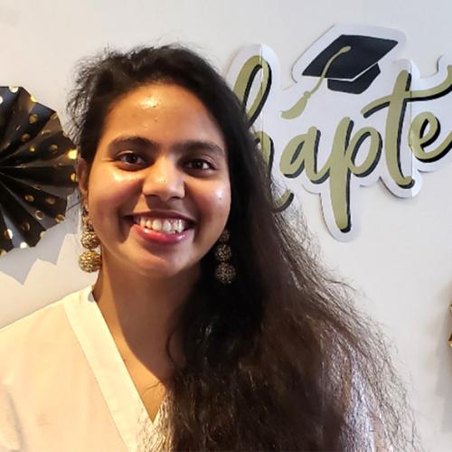 Dariya Darvin smiles as she stands in front of a backdrop with symbols of graduation such as an academic hat.