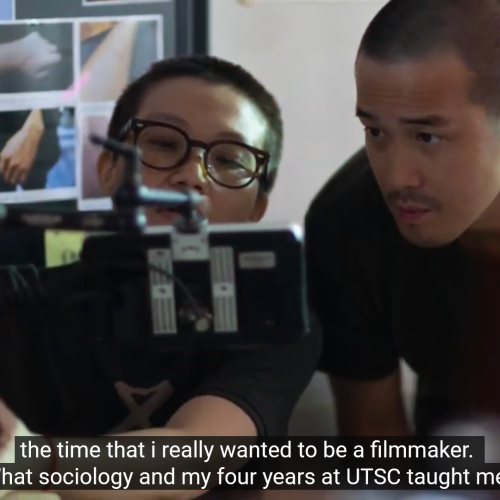 In a still from a video, Derek Tsang looks into the viewfinder of a camera.