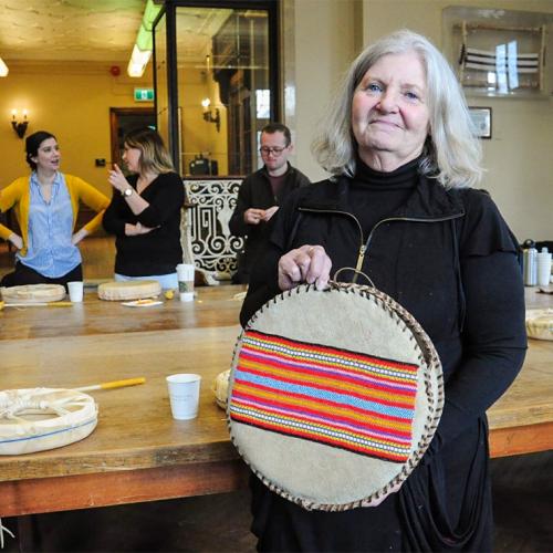 Elder Constance Simmonds smiles as she holds a flat drum top decorated with embroidery and still being stitched on the edges.