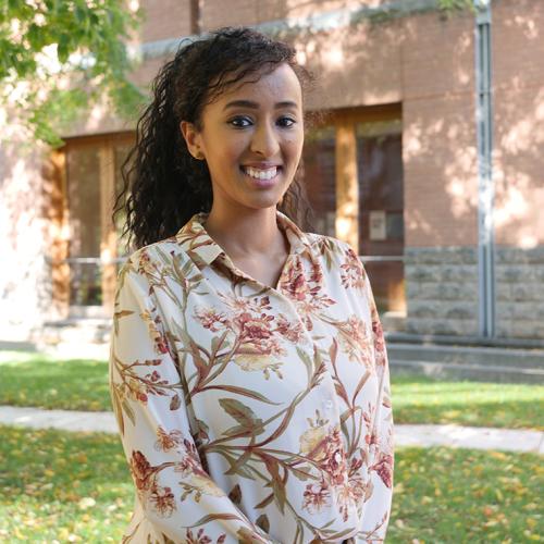 Entisar Yusuf smiles as she stands in a sunny courtyard under a tree.