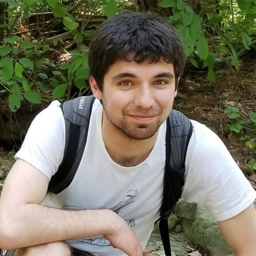Erik Etzler smiles as he crouches on a forest trail, wearing a backpack.