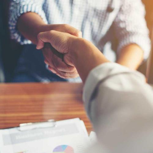 Picture of the arms and hands of two people shaking hands across a wooden desk.