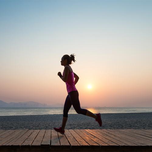 A woman runs along an empty beach at sunset.