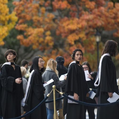 Graduates line up outside Convocation Hall in front of the fall foliage