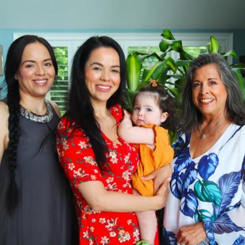 Cynthia Wesley-Esquimaux smiles as she stands next to her two daughters, one holding her own small daughter.