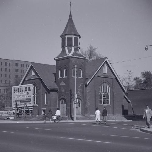 Archival photograph of First Baptist Church in the 1950s, squeezed next to a construction site and a billboard for Shell Oil.