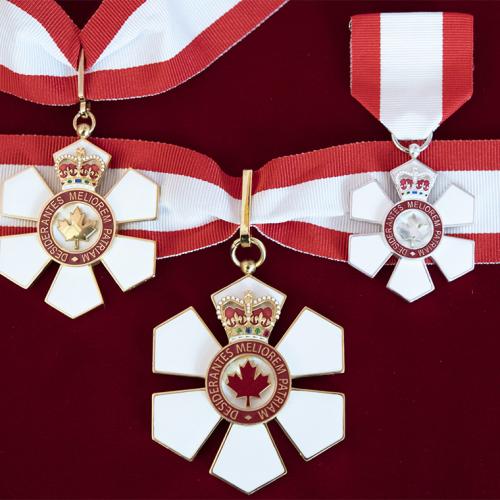 Three six-petalled Order of Canada medals hanging on ribbons in the colours of the Canadian flag.